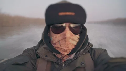 Man in warm clothes, hat, glasses and a mask on his face rides in a fishing boat Stock Footage 127005831