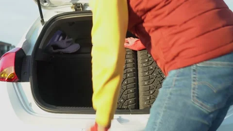 A man in warm clothes puts in a car trunk studded winter tires Stock Footage 163796111