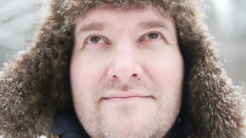 A man in a warm hat with earflaps stands in a winter park Stock Footage 100026721