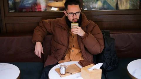Man in a warm jacket drinking matcha on a cozy cafe terrace on an autumn  Foto stock
