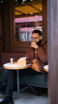 Man in a warm jacket drinking matcha on a cozy cafe terrace on an autumn  Stock Photos