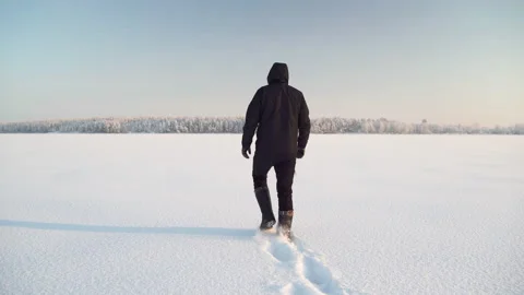 A man in warm winter clothes walks along a lake covered with ice and snow Stockbeeldmateriaal 146327900