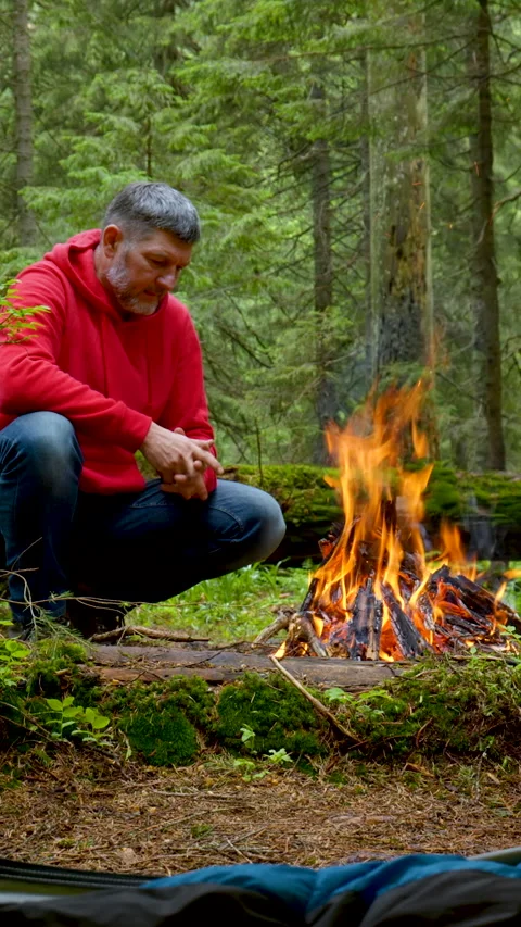 Man warming hands by campfire in forest wilderness Stock Footage 336046896
