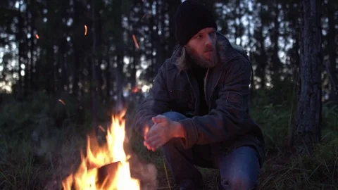 Man warming his hand by the fire in a forest Stock Footage 76357401