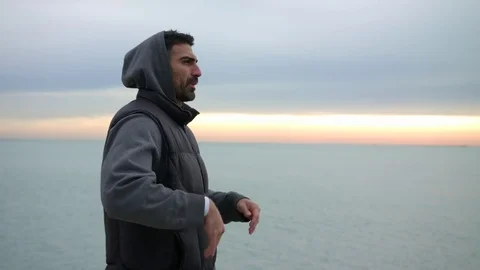 Man is warming up his hands by breathing at the cold morning seaside. Morning Stock-Footage 82649364