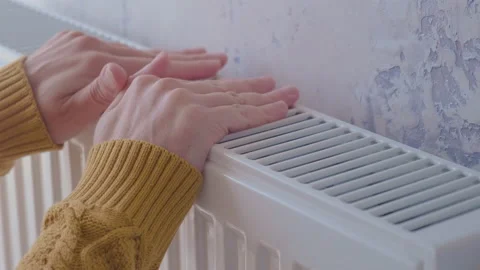 Man warming his hands in yellow sweater on the heater at home Stock Footage 231236862