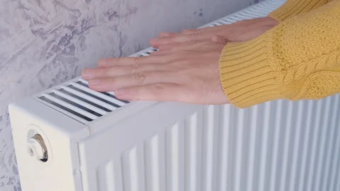Man warming his hands in yellow sweater on the heater at home during cold winter Stock Footage 254514796