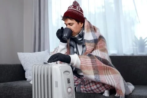 Man warms hands by a heater in cold weather. He drinks hot tea, facing a ho.. Stock Photos