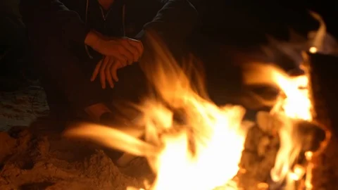 A man warms himself by the fire at night on the shore Stock Footage 115992936