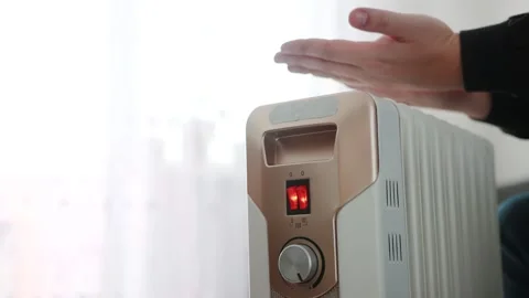 A man warms his hands and palms over an electric radiator heater. The concept of Stock Footage 253470269