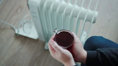 A man warms his hands on a cup of hot tea against the backdrop of an electric Stock-Footage 255634579