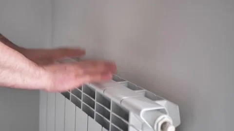 Man warms his hands from a heating radiator Stock Footage 198921033