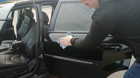 The man washes the black car.The guy wipes the glass and the car door with a rag Stock Footage 140268899