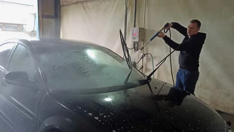 The man washes the black car.The guy is watering the car with a hose. Stock-Footage 140659423