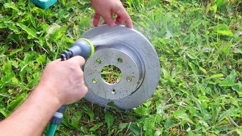 Man washes car brake disc with water from a hose against a background of grass Vídeos de archivo 140916144