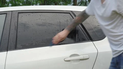 A man washes the car windows with a cloth before applying an anti-rain coating. 库存影片 336913930
