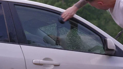 A man washes the car windows with a cloth before applying an anti-rain coating. 库存影片 336914036