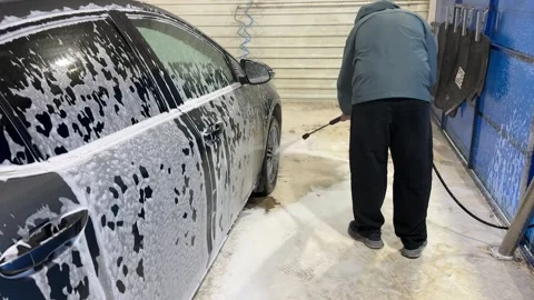 A man washes foam off a car with a high-pressure cleaner Stock Footage 308818892