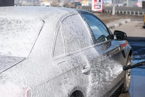 A man washes off the foam while washing the car. Stock Photos