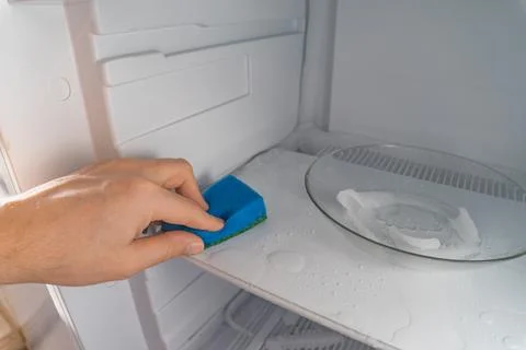A man washes the freezer using sponge. Cleaning the refrigerator. Selective Stock Photos