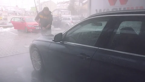A man washes the front of his dark gray car with a hose in a self-service car Stock Footage 77299839