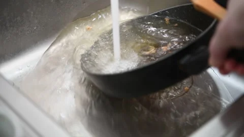 A man washes a frying pan in the kitchen sink. Video stock 299721658