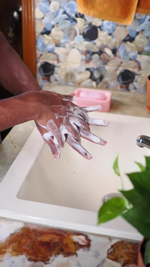 Man washes hands with soap in a bathroom sink with a plant nearby Stock Footage 346513865