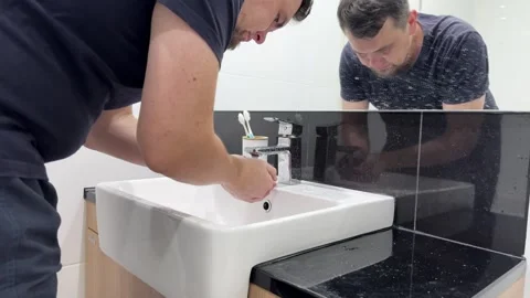 A man washes his face in the bathroom sink while preparing for the day. Stock-Footage 305636971