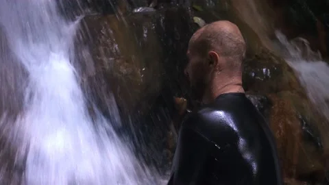 A man washes his face in a waterfall. A large stream of water falls on the man. Stock-Footage 133460642