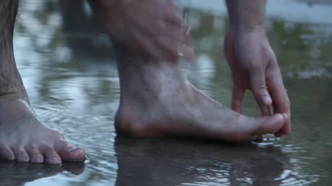 A man washes his feet in a puddle on a summer day after the rain Stock Footage 265200220