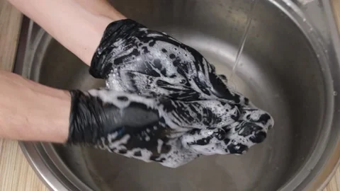 A man washes his hands in black rubber gloves in the sink under the water tap. T Stock Footage 152527560