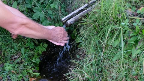 A man washes his hands in a mountain stream. Stock Footage 149078196