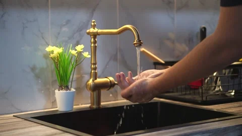A man washes his hands under a decorative faucet in the kitchen. 動画素材 329851489