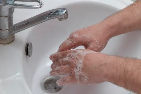 A man washes his hands in a white washbasin. An open tap, running water, soap Stock Photos