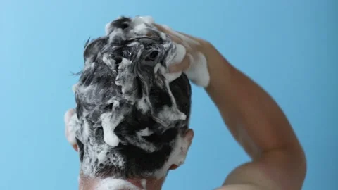 A man washes his head with shampoo on blue background. Stock Footage 137483056