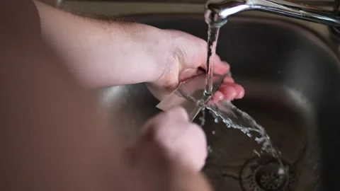 Man washes a large knife under running water in a metal sink. Stock Footage 260264753