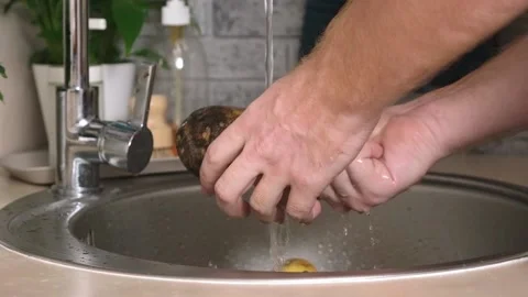 A man washes a potato from ground under a stream of tap water for further Stock Footage 224515958