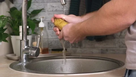 A man washes a potato from ground under a stream of tap water for further Stock Footage 229928395