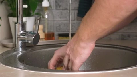 A man washes a potato from ground under a stream of tap water for further Stock Footage 230721514