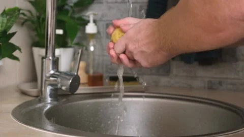 A man washes a potato from ground under a stream of tap water for further Stock Footage 231185227
