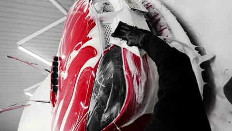 Man washes a red Subaru at a car wash. Wipes the headlight and bumper of the car Vídeos de archivo 235873246