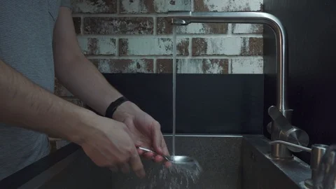 A man washes a spoon with a cleaning sponge in the kitchen Stock Footage 102223034