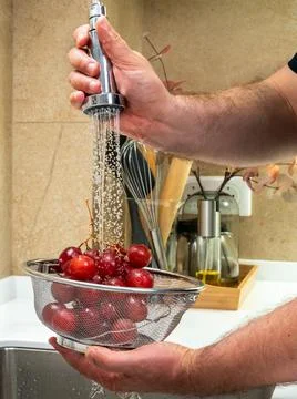 A man washes table grapes under a strong spray of water Stock Photos