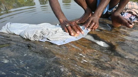 A man is washing clothes by hand on a stone at the riverbank. Video stock 333025610
