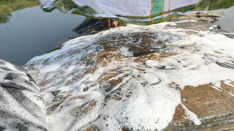 A man is washing clothes by hand on a stone at the riverbank. Video stock 333025816