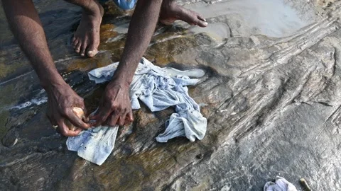 A man is washing clothes by hand on a stone at the riverbank. Video stock 333025983