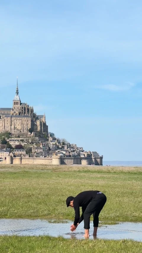 Man Washing Hands in Stream with Mont Saint-Michel Abbey in Rural France Stock Footage 342183948