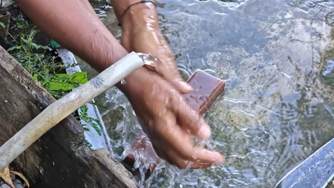 Man Washing Hands Under Flowing Water in Simple Outdoor Setting Stock Footage 322871012