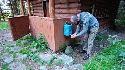 Man Washing Hands Using Outdoor Water Dispenser by Wooden Cabin Video stock 344893653