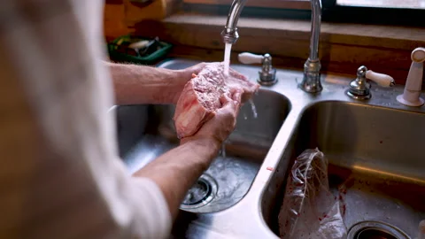 Man washing a large piece of beef under running water in a sink Stock Footage 145745245